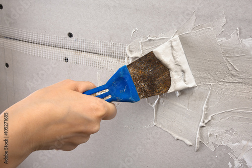 spatula with plaster in hand during plastering walls, closeup