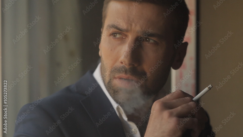Young man smokes a cigarette at the window Young man smokes a cigarette at the window