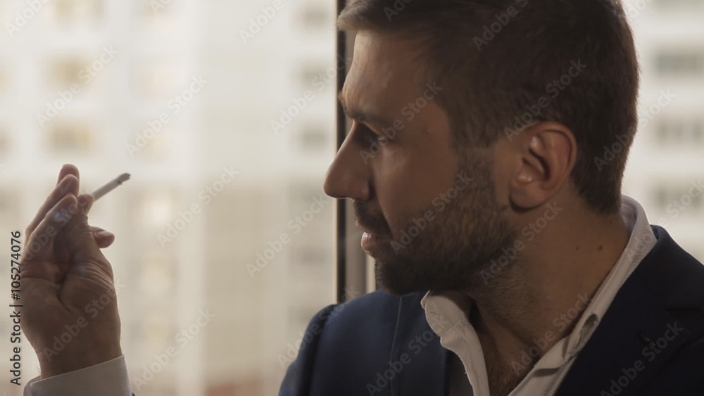 Young man smokes a cigarette at the window Young man smokes a cigarette at the window