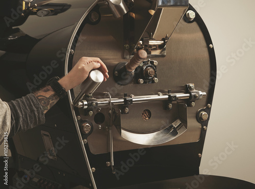 Fotografija Tattooed hand pulls lever in coffee roasting machine