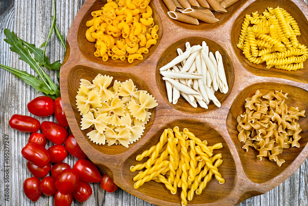Various mix of pasta and small red tomatoes on wooden bowl Various mix of pasta and small red tomatoes on wooden bowl