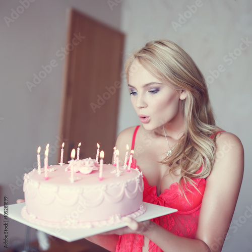Sexy blonde woman blowing candles on cake in lingerie