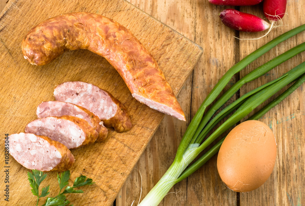 Piece of sausage and slices decorated with green parsley on wood Piece of sausage and slices decorated with green parsley on wood