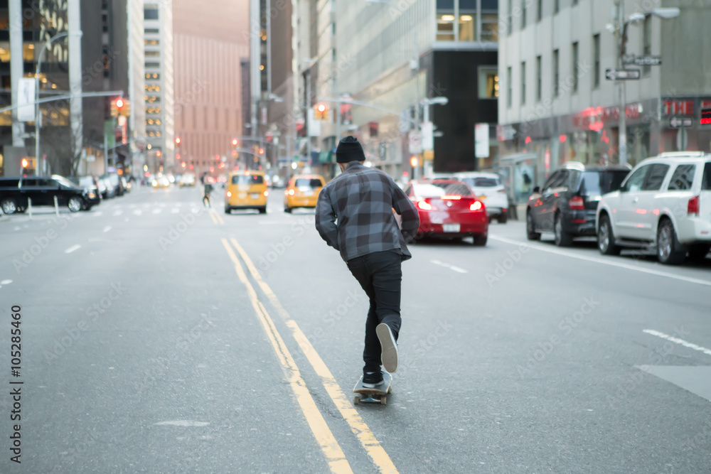 Back figure of young skateboarder cruising down the city street