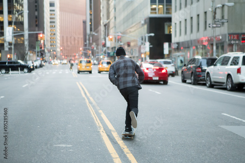 Back figure of young skateboarder cruising down the city street © goofyfoottaka