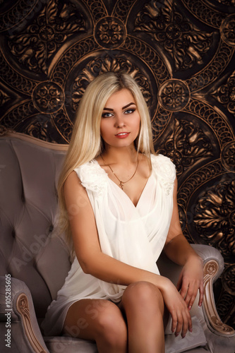 sexy blonde in a white dress sits on a chair