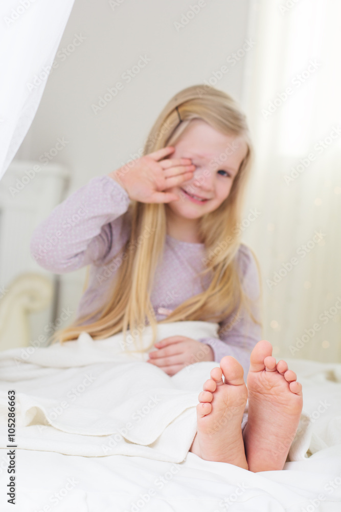 Happy child girl is sitting and yawning in the bed