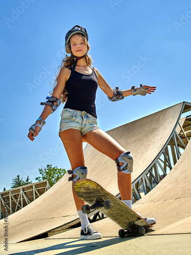 Portrait of teen girl standing on his skateboard aganist blue sky outdoor. Skate sport.