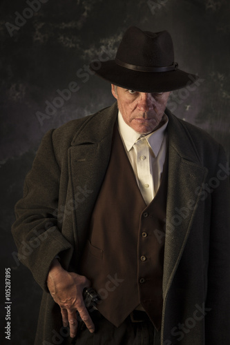 Photography Sinister/Low key image of man in overcoat & hat in sinister pose with hand on gu