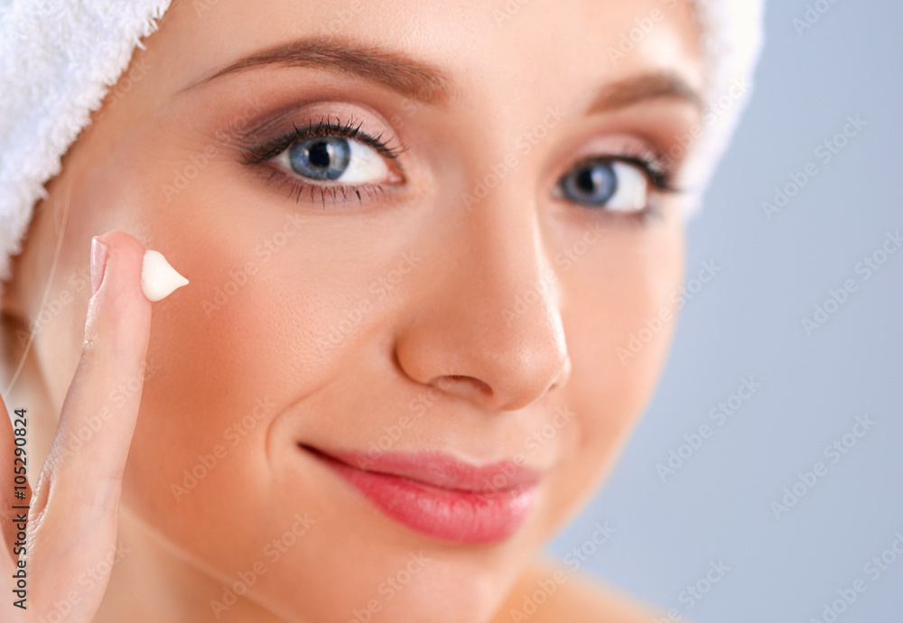 Beautiful young woman applying a creme on her face isolated on gray background Beautiful young woman applying a creme on her face isolated on gray background