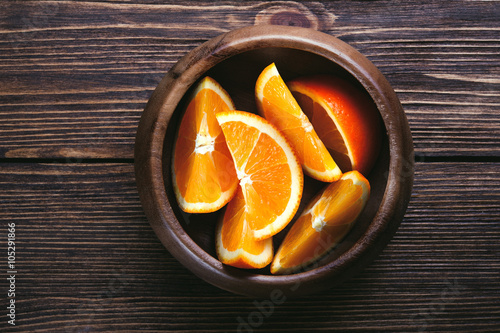 Slices of orange wooden bowl on wooden table. Top view. Toned