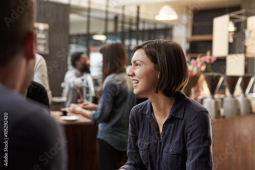 Brunette woman smiling and looking away in a busy cafe