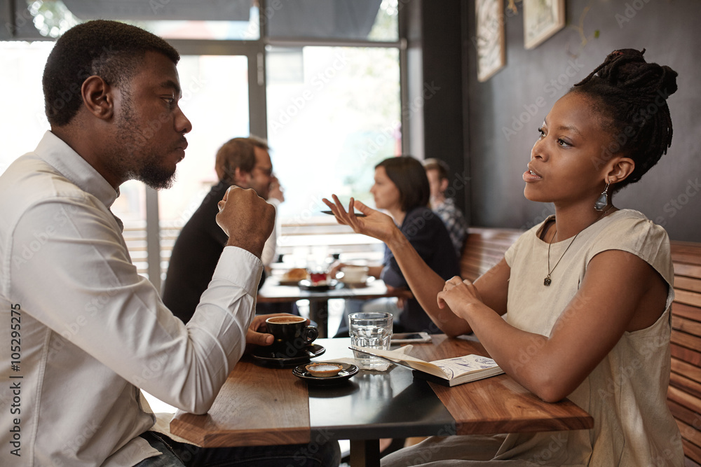 African woman and man discussing business ideas at busy cafe