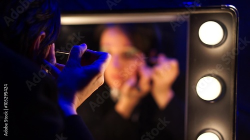 Actress applying makeup in front of the mirror in the dressing room.