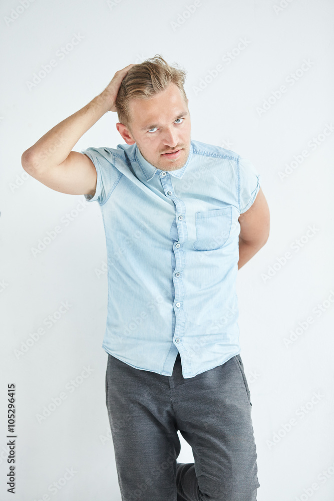 Brutal man with a small beard is leaning on the wall , wearing a blue short-sleeved shirt and gray pants , hands are behind his back Brutal man with a small beard is leaning on the wall , wearing a blue short-sleeved shirt and gray pants , hands are behind his back