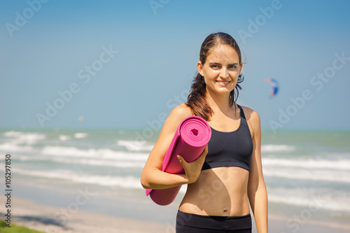 Молодая женщина с ковриком для йоги на фоне моря и голубого неба