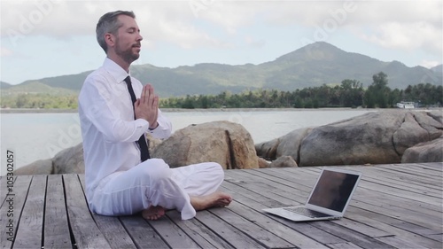 businessman doing yoga on a wooden bridge with a laptop
