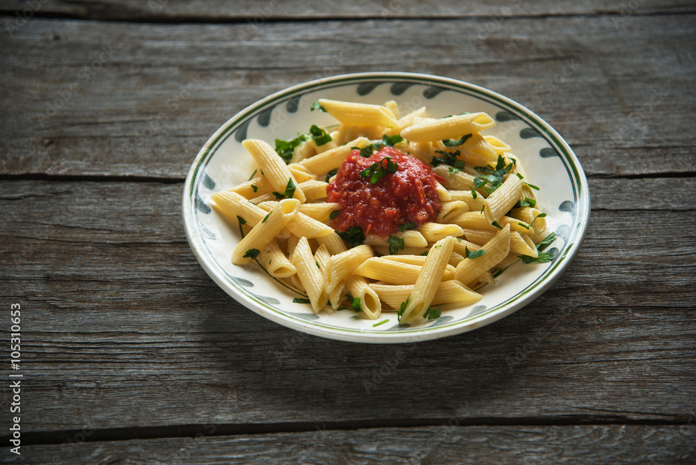 Penne pasta in tomato sauce, tomatoes decorated with parsley on a wooden background Penne pasta in tomato sauce, tomatoes decorated with parsley on a wooden background