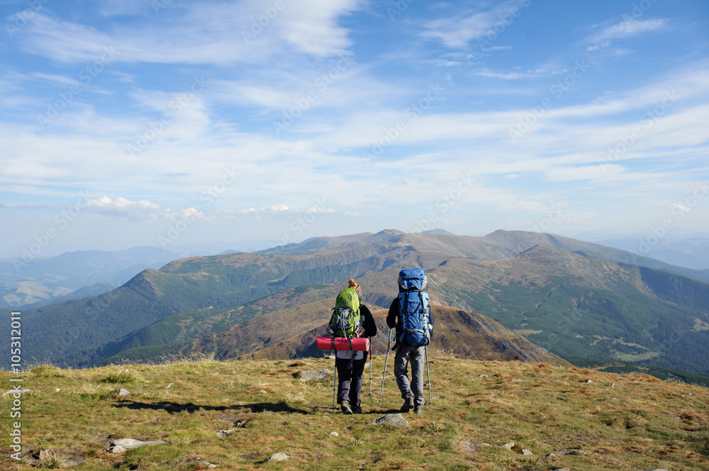 Young couple walking together on the mountain summit enjoying beautiful open panoramic view and their hike together. Hiking gear/equipment. Man and woman using trekking sticks.