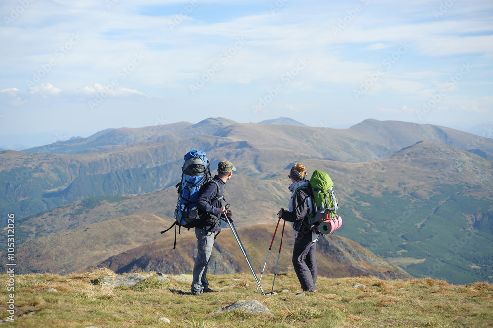 Young couple standing together on the mountain summit enjoying beautiful openview in nature during hiking travel. Hiking gear/equipment. Man and woman using trekking sticks.
