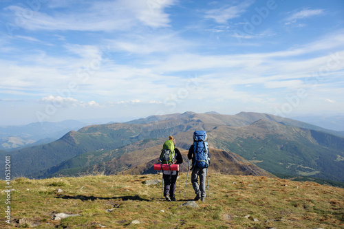 Young couple walking together on the mountain summit enjoying beautiful open panoramic view and their hike together. Hiking gear/equipment. Man and woman using trekking sticks. © anatoliy_gleb