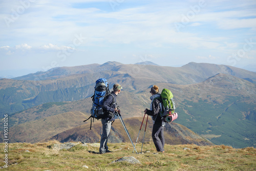 Young couple standing together on the mountain summit enjoying beautiful openview in nature during hiking travel. Hiking gear/equipment. Man and woman using trekking sticks.