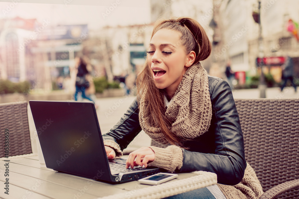 Beautiful young student using laptop at outdoor cafe / Portrait of beautiful smiling woman sitting in a cafe with laptop outdoor Beautiful young student using laptop at outdoor cafe / Portrait of beautiful smiling woman sitting in a cafe with laptop outdoor