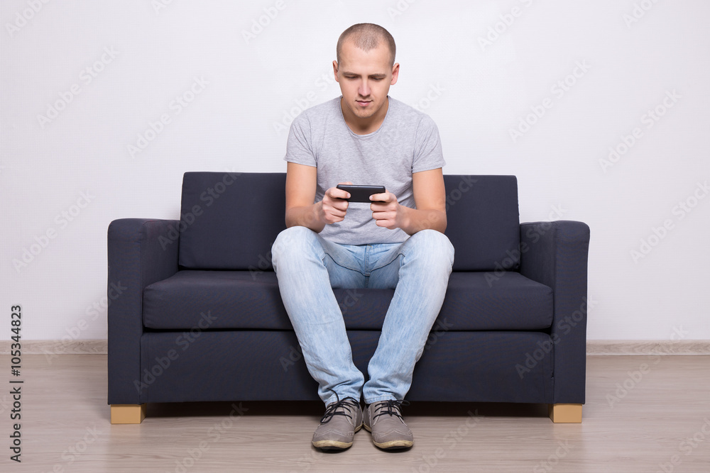 young handsome man sitting on sofa with mobile phone