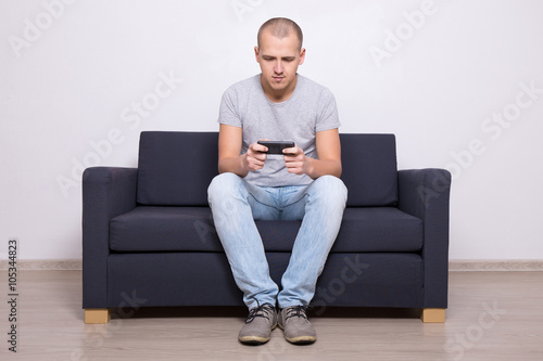 young handsome man sitting on sofa with mobile phone