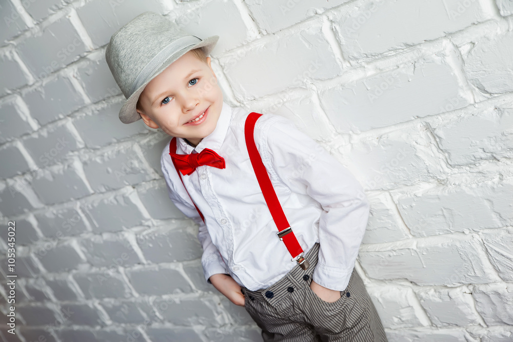 little boy wearing a red bow tie, suspenders and white shirtand against