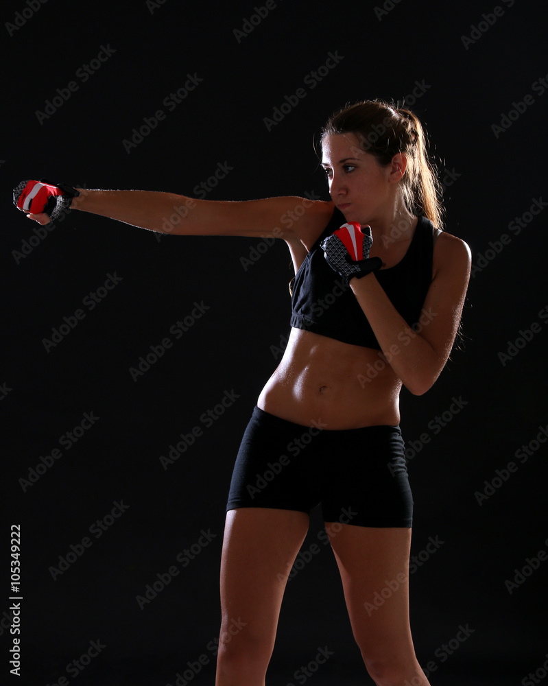 Fitness woman punching and wearing red training gloves. Black background Fitness woman punching and wearing red training gloves. Black background