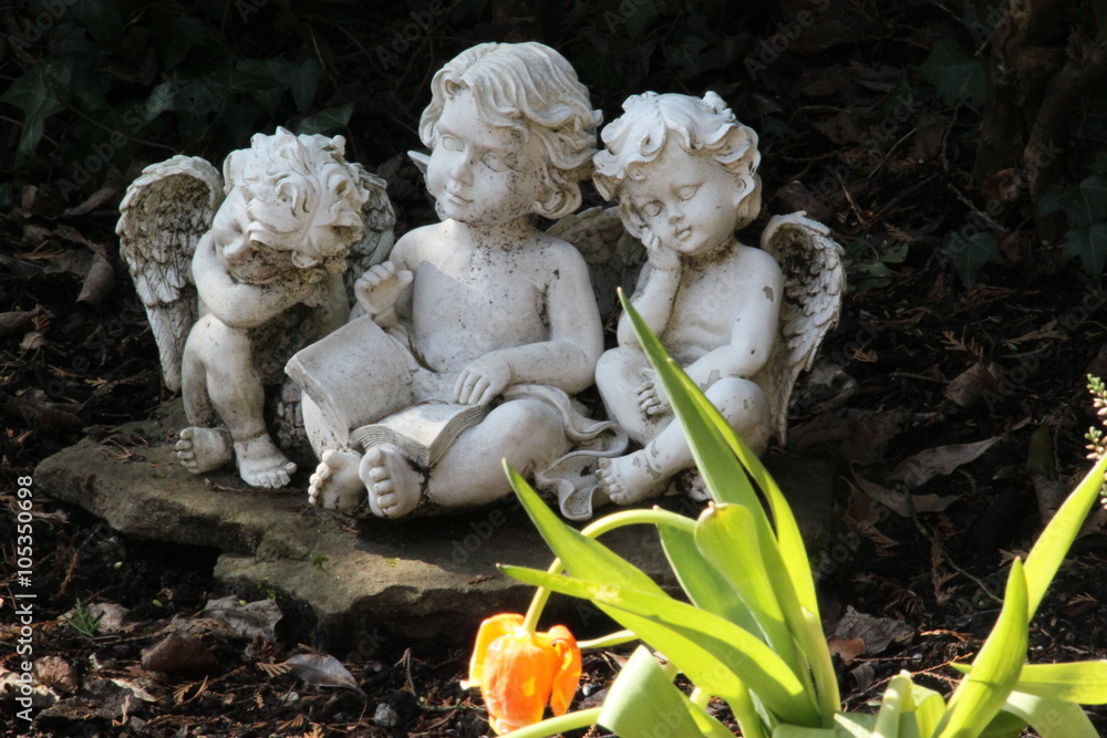 Drei Engel sitzen auf einm Grab neben Tulpe, die verwelkt ist