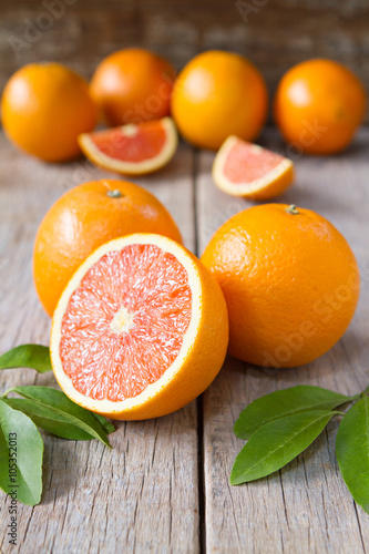 Fresh oranges with slices and leaves on wooden background. Selective focus.