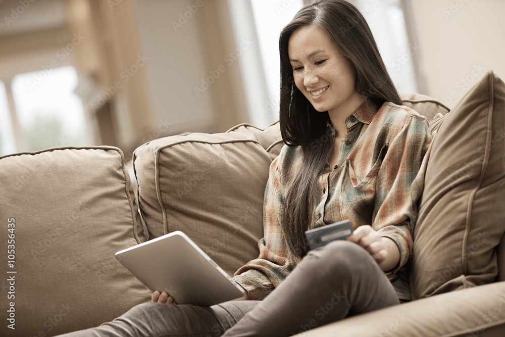 A woman sitting on a sofa at home holding a digital tablet and a credit card, shopping online, A woman sitting on a sofa at home holding a digital tablet and a credit card, shopping online,