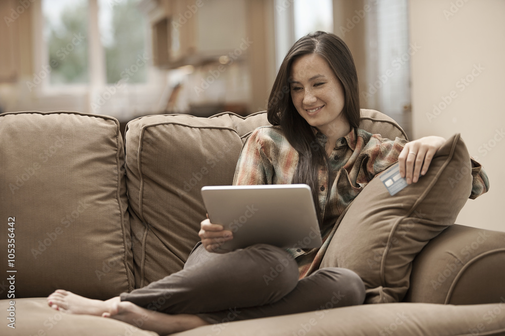 A woman sitting on a sofa at home holding a digital tablet and a credit card, shopping online, A woman sitting on a sofa at home holding a digital tablet and a credit card, shopping online,