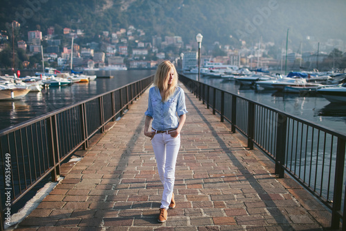 blonde girl walks on the pier of a mountain lake como italy