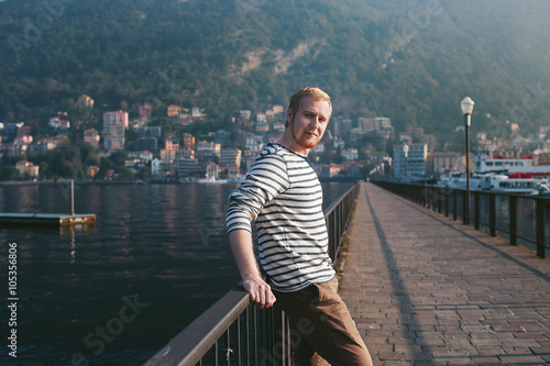 bearded man standing on the pier of a mountain lake Como