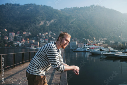 bearded man standing on the pier of a mountain lake Como