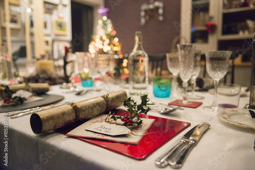 A table laid for a Christmas meal, with silver and crystal glasses and a Christmas tree in the background,  photo