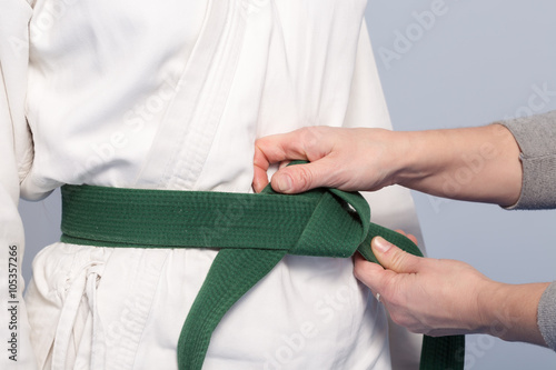 Hands of a parent who helps a child to tietie a green belt for martial arts training