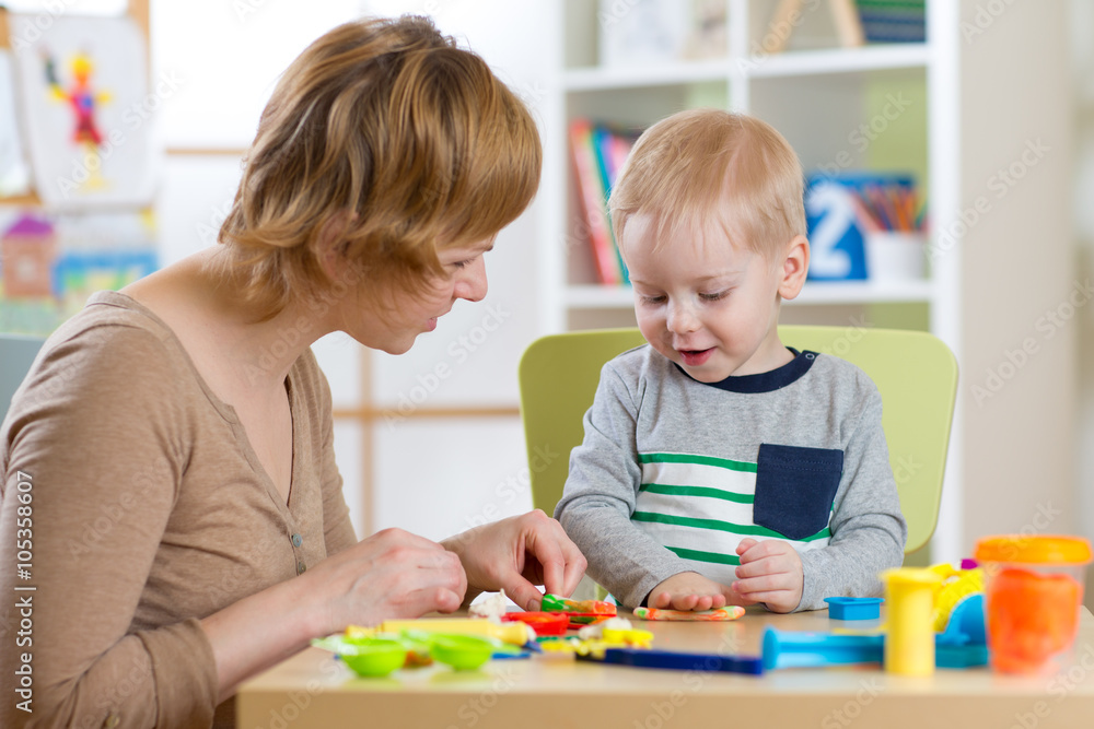 Woman and kid boy playing with plasticine at table in nursery room Woman and kid boy playing with plasticine at table in nursery room