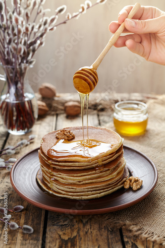 Flowing honey on stack of traditional american pancakes with nuts. Delicious lunch on vintage wooden table background.