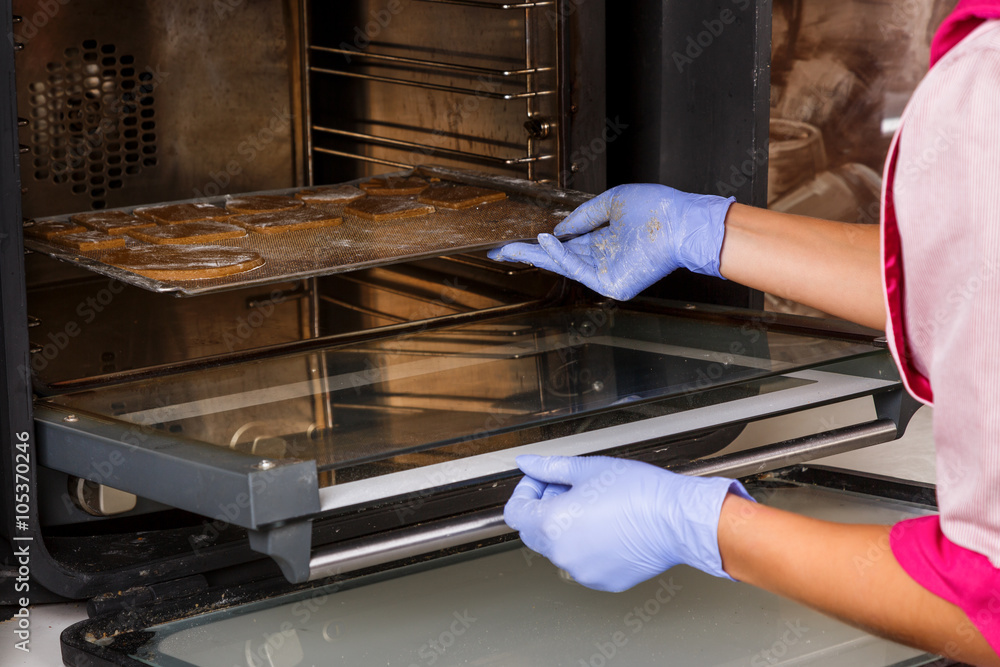 Female confectioner puts dripping pan with cookies into the oven Female confectioner puts dripping pan with cookies into the oven
