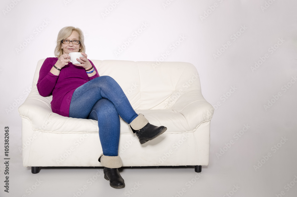 Senior woman sitting on a white sofa and drinking tea. Senior woman sitting on a white sofa and drinking tea.