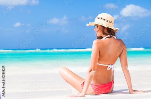 back view of long haired girl in stripy swimsuit and straw hat on tropical caribbean beach