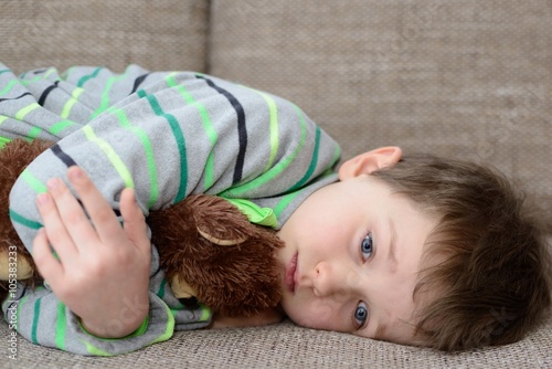 child hugs his teddy bear and lying on the sofa