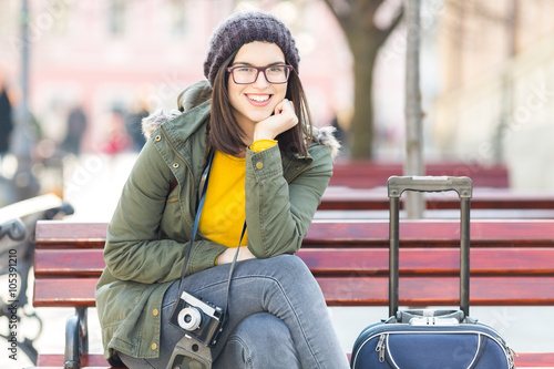 Young woman resting on a bench. She is on vacation and carring camera and sutcase. photo