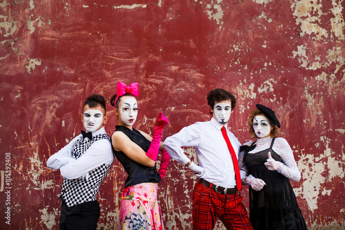 Four mimes standing firmly against the backdrop of a red wall.