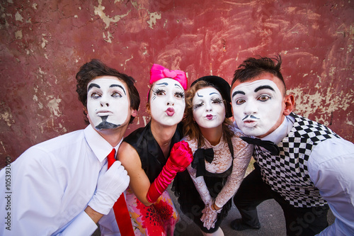 Four mimes cute pose in front of a red wall.
