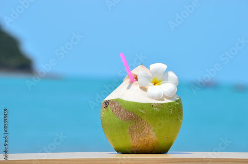 Tropical green coconut with drinking straw on wood table against
